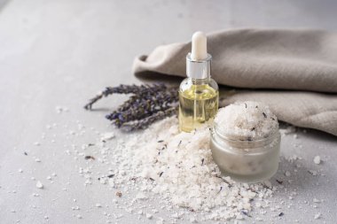 Lavanta banyosu ürünleri ve aksesuarlar serpilmiş tuz ve bitki filizi ile hafif bir arka planda düzenlenmiştir.