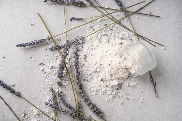 Lavanta banyosu ürünleri ve aksesuarlar serpilmiş tuz ve bitki filizi ile hafif bir arka planda düzenlenmiştir.