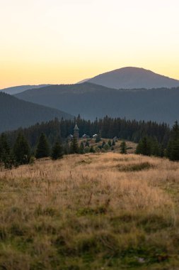 Yoğun ormanlar ve yuvarlanan tepelerle çevrili sakin bir dağ köyünün üzerinde gün batımı. Ukrayna 'daki Karpat Dağları' nda yürüyüş 