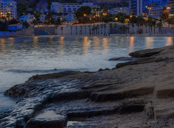Beautiful view of the night sea. Lights glow in high-rise buildings. Water is blurred. Beautiful wet stone in the foreground.High quality photo