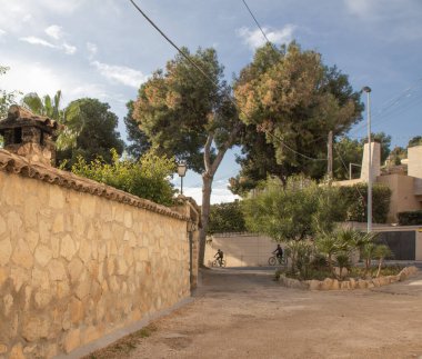 Avrupa 'da bir tatil köyünün çiçek tarhlı ve taş duvarlı avlusu. Arka planda bisikletçiler var. Yüksek kalite fotoğraf