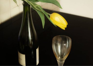 Cam masadaki bir şişe şarabın üzerinde sarı bir lale yatıyor. Yakınlarda kristal bir cam var. Yüksek kalite fotoğraf