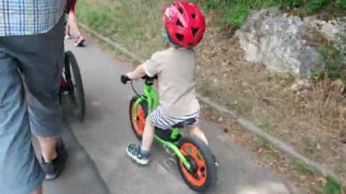 Kasklı bisiklet süren küçük bir çocuk.