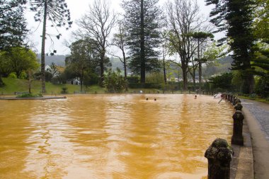 Portekiz, Azores 'deki ikonik turuncu termal havuz, mineral zengini volkanik sularıyla, tarihi binalar ve yemyeşil bitki örtüsüyle çevrili..