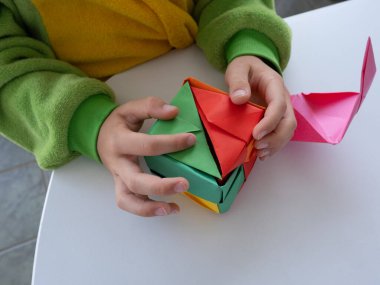 Çocuk beyaz arkaplanda parlak kağıttan yapılmış katlanmış bir origami küpü açıyor.