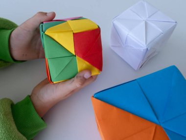 Masanın üzerinde katlanmış origami küpleri olan el yapımı bir kağıt bloğu tutan çocuk.
