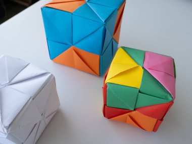 Asgari gölgeli beyaz bir yüzeye yerleştirilmiş parlak modüler origami küpleri.