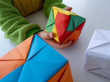 Neşeli bir öğrenme etkinliğinde canlı origami şekilleri ve blokları tutan çocuk.