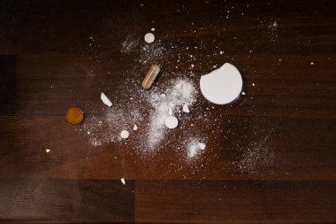 Çeşitli tabletler, kapsüller ve beyaz toz koyu ahşap bir zemine saçılmış ilaç, sağlık ve aksiliği simgeliyor..
