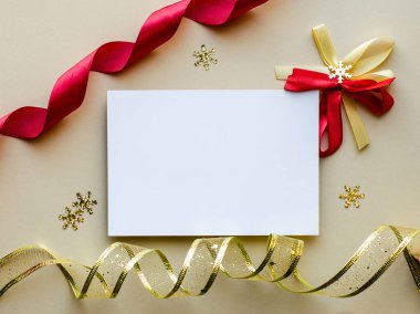 Bu büyüleyici Noel kartı modeli, dekoratif kar taneleriyle tamamlanmış, kırmızı ve altın renkli şenlikli kurdelelerle süslenmiş boş bir beyaz kart içeriyor. Bayram kutlamaları ve davetiyeler için mükemmel..