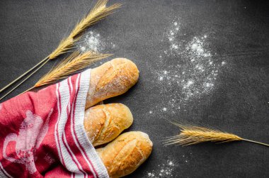 A beautifully styled image featuring freshly baked baguettes wrapped in a red striped towel, accompanied by wheat stalks and sprinkled flour. The rustic setup evokes a warm, homemade feel clipart