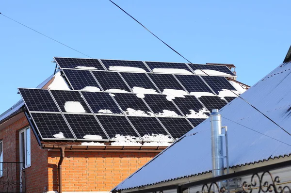 Snow-covered solar panels are mounted on the roof of a private house. Alternative energy in winter.