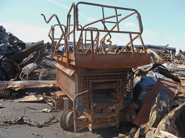 A burnt construction mobile lift among a pile of building debris and rusted metal. Remains after the fire.