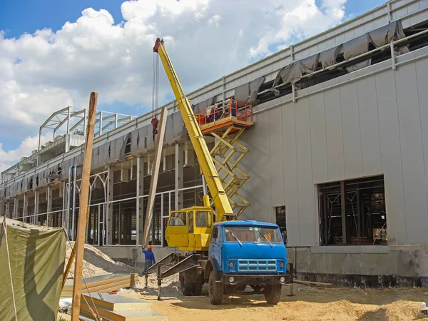 Construction of a large logistics warehouse with refrigerating chambers. A construction site with a crane that lifts a sandwich panel for installation