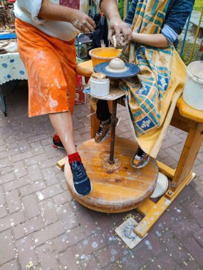 Çömlek yapıyorum. Çömlek çarkında kil çömlek üzerinde çalışan bir ustanın ve öğrencinin elleri. Poz verilmemiş sokak fotoğrafı, festival sahnesi.