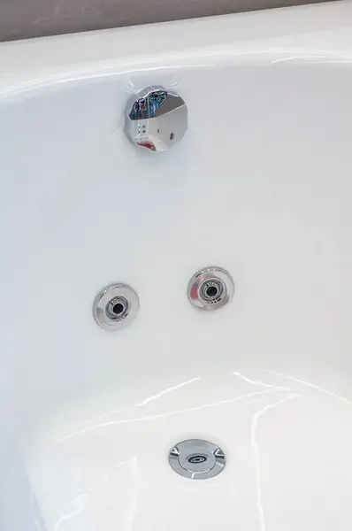 Stock image Detail view of an acrylic bathtub with chrome water jets and a drain plug.