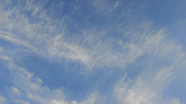 stock image Expansive blue sky with delicate white clouds, creating a serene and open atmosphere. The clouds are thin and wispy, adding texture to the clear sky.