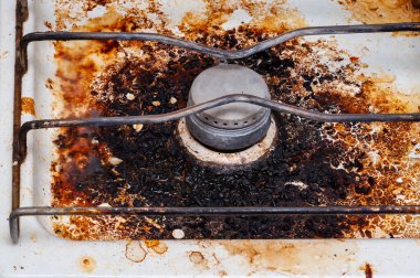 Kirli ve yanmış bir gaz sobası yüzeyine yakın çekim. Lekeler ve yiyecek artıklarıyla. Yanmış ve yağlı gaz sobası yüzeyinde ağır toprak ve lekeler var..