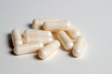 Temiz, beyaz bir yüzeye beyaz kapsül yığını, vitamin veya takviyeleri sembolize eder..