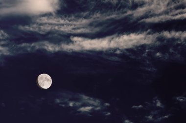 Ay, karanlık ve bulutlu bir gökyüzünü aydınlatarak atmosferik ve kasvetli bir gece sahnesi yaratır..