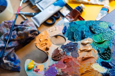 Renkli bir palet, araçlar ve boyalardan oluşan bir ressamların çalışma alanının yakın çekimi.