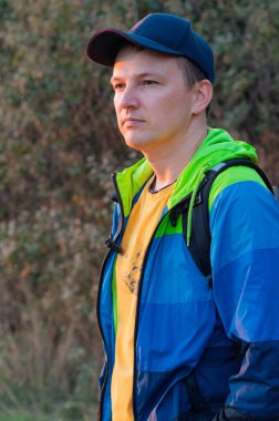 Renkli ceketli bir gezgin, sakin bir ifadeyle ayakta duruyor. Hem fiziksel bir yolculuğu hem de doğada sessiz bir iç gözlem anını temsil eder..