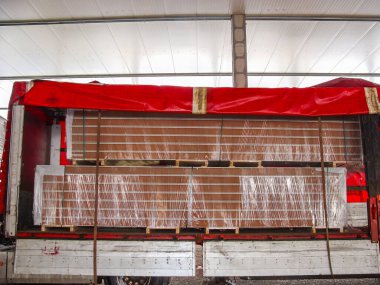 İnşaat alanındaki kırmızı bir tırın içinde paketlenmiş sandviç panelleri. İnşaat malzemeleri bir depo projesi için bir kamyonla taşınıyor..