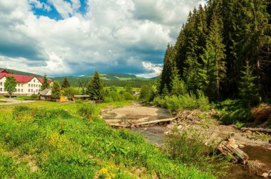 Canlı yeşil bir vadiden geçen sığ bir derenin yer aldığı pitoresk bir dağ manzarası..