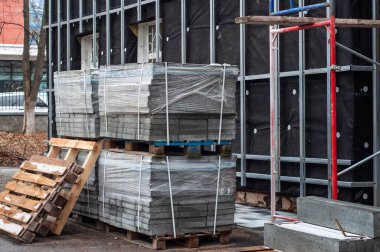 Plastiğe sarılı asfalt yığınları bir inşaat sahasında paletlerin üzerinde, yürüyüş yolları oluşturmak için kullanılmaya hazırlar..