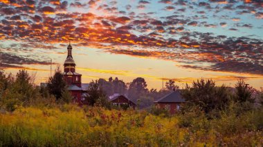 Gün doğumu gökyüzünü canlı renklerle boyar, büyüleyici bir kilise ve huzur dolu bir manzaraya yerleşmiş evler üzerine sıcak bir ışıltı saçar..