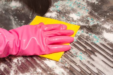 Pembe eldivenli bir ele yakından bak. Kir ve sabun kalıntılarını temizlemek için sarı bir süngerle desenli bir metal yüzeyi temizle. Temizlik ve hijyene odaklan..