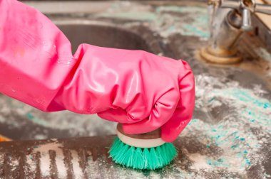 Pembe eldiven takan ve yeşil fırça ve temizlik ürünüyle eski, lekeli bir lavaboyu fırçalayan birine yakından bakın..