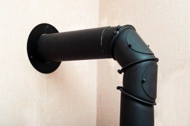 Siyah metal baca borusu, odun sobası için bir egzoz yolu sağlar ve açık pembe bir duvara karşı oturur..