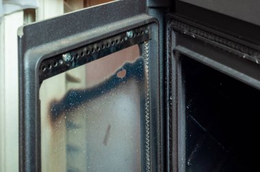 Close-up of a used and dirty black fireplace door that is slightly ajar, providing a glimpse into the dark interior of the firebox. clipart