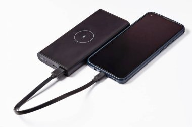USB kablosu kullanan bir akıllı telefon bir güç bankası tarafından şarj ediliyor. Cihazlar beyaz bir yüzeyde izole edilmiş..