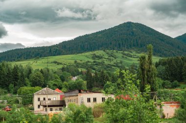 Bulutlu bir gökyüzünün altındaki ormanlık bir dağ sırasının altındaki vadide yuva yapmış tuhaf bir köy huzuru çağrıştırıyor..