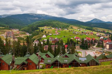 Ukrayna Karpatları 'ndaki bir dağ köyünün manzarası. Gökyüzü bulutlu, kayak asansörleri ve yemyeşil ağaçlar..