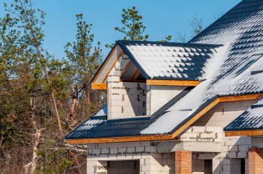 Bir evin inşaatı devam ediyor, kar çatıyı hafifçe temizliyor ve açık mavi gökyüzünün altındaki blok duvarlar....