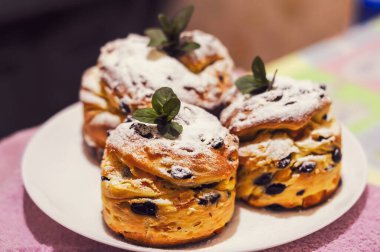 Üç iştah açıcı kulich keki pudra şekerle kaplanmış ve taze nane yapraklarıyla süslenmiş, bayramlık bir yemek sırasında paylaşmaya hazır..