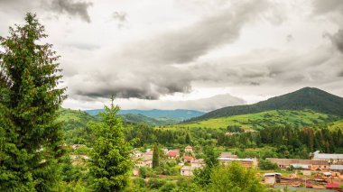 Vadideki köyün üzerinde bulutlu bir gökyüzü. Orman ve evler uzaktan görülebilir. Dağ vadisinin güzel manzarası.