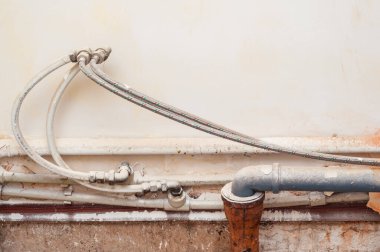 Duvarın arkasındaki eski ve tozlu tesisat borularının manzarası. Tesisat sisteminin karmaşıklığını ve bakım ve onarım ihtiyacını gösterir.