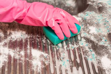Beyaz tozla kaplı bir yüzeyi temizlemek için pembe koruyucu eldiven takan yeşil bir sünger kullanan birinin yakın çekimi..