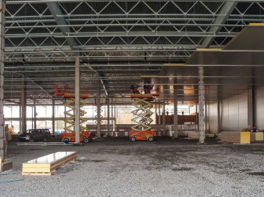 İşçiler inşaat halindeki yeni bir deponun tavanına çakıl döşemeli paneller yerleştirmek için makas asansörleri kullanıyorlar..