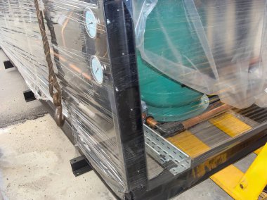 Nakliye için plastiğe sarılı büyük bir endüstriyel ekipman yan tarafında metal bir kanca olan bir palete yerleştirilmiş..