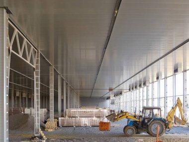 Ön yükleyicisi olan bir traktör, boş bir depo şantiyesinde çalışmaya hazır bir şekilde sahneleniyor..