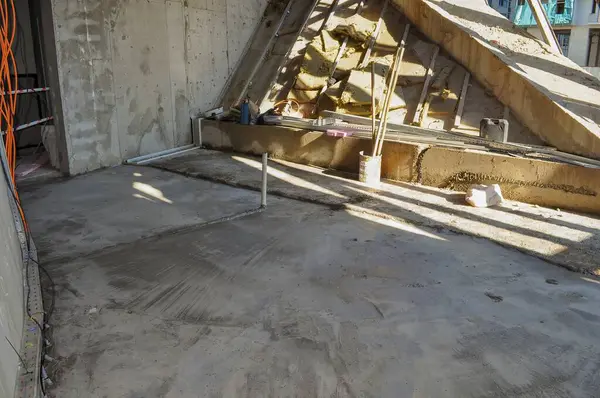 Görüntü, inşaat halindeki tamamlanmamış bir odayı yakalıyor, çıplak beton duvarlar, döşeme ve tavandaki yalıtım malzemelerini ortaya çıkarıyor..
