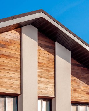 Mimari detaylar modern bir ev ahşap kaplama, sıva sütunlar, çatı çizgisi ve açık mavi gökyüzüne karşı minimalist tasarım gösteriyor.