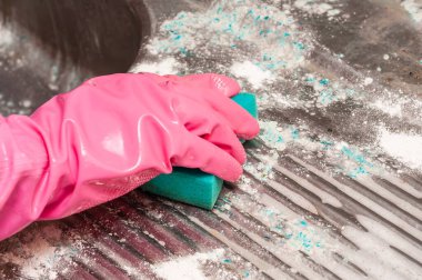 Beyaz deterjanla kaplı metal bir süpürgeyi temizlemek için yeşil sünger kullanan ve pembe eldiven giyen birinin yakın plan fotoğrafı..