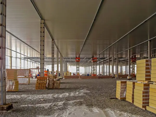 Bina inşaat halinde, malzemeler sahneleniyor ve işçiler uzaklardan görülebiliyor, metal ve beton yapıları var..