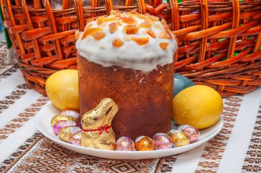 13 Mart. 2024. Poltava, Ukrayna. Bayramlık Paskalya Kulich keki, yumurta ve çikolatalı tavşancık, geleneksel bir masa örtüsünün arka planında..